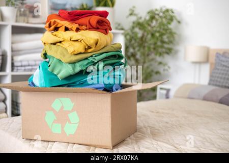 Ein Stapel Kleidung in verschiedenen Farben in einer Schachtel mit einem Recycling-Schild. Stockfoto