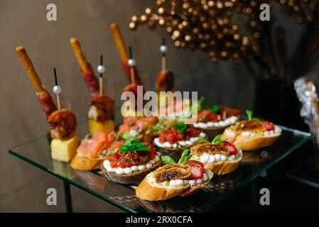 Kanapees auf einem Glastisch. Kanapees mit verschiedenen Käsesorten, Tatar, Lachs, Salsa, Tomaten, Mozzarella. Luxuriöses Catering. Stockfoto