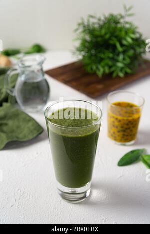 Ein grüner Smoothie mit Passionsfrucht-Fruchtfleisch und Spinatblättern und einem Wasserkrug. Gesunder grüner Smoothie, erfrischendes Diätgetränk auf weißem Rücken Stockfoto