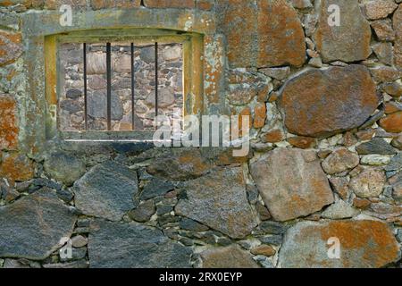 Ein vergittertes Fenster in einer Steinmauer mit Ziegelrand Stockfoto