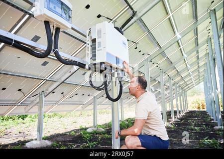 Männlicher Arbeiter, der prüft, ob der Solarwechselrichter richtig funktioniert. Junger Mann, der Wechselrichter konfiguriert. Rückansicht der Photovoltaikbatterie. Stockfoto