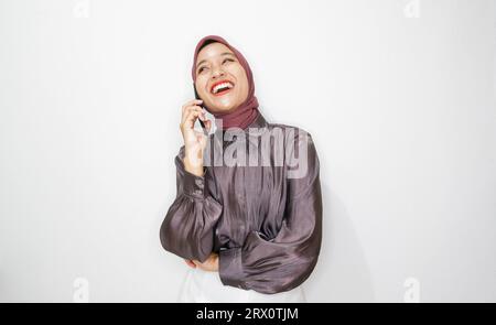 Porträt einer glücklichen jungen muslimischen Frau, die auf dem Handy vor weißem Hintergrund spricht Stockfoto