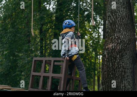 Teenager-Boyin Outdoor-Abenteuerpark, der Hindernisparcours passiert. Hochseilpark. Hochwertige Fotos Stockfoto