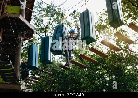 Teenager-Boyin Outdoor-Abenteuerpark, der Hindernisparcours passiert. Hochseilpark. Hochwertige Fotos Stockfoto