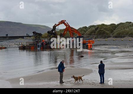 Barmouth, Großbritannien, 21. September 2023. Die Arbeiten wurden gestern fortgesetzt, um alte Abschnitte der Barmouth-Eisenbahnbrücke zu entfernen, nachdem die Unwetter die Arbeiten um drei Tage verschoben hatten. Die berühmte, 157 Jahre alte, unter Denkmalschutz stehende Struktur am Mawddach Eastuary befindet sich in der Endphase eines dreijährigen Wiederaufbauprojekts im Wert von 30 Millionen Pfund. Die Doppelstahlspanner werden durch identische neue Strukturen ersetzt, die vorübergehend verwendet werden, um Kräne zu halten, die Abschnitte der alten korrodierten Brücke auf Pontons unten unterbauen. Leute, die ihren Hund am Strand laufen, beobachten, wie Teile der Brücke zur Entsorgung abgeschnitten werden. G.P. Essex/Alamy Live News Stockfoto