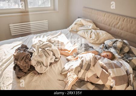 Hausreinigung. Ein glückliches kleines Mädchen, die Helferin hat Spaß und lächelt, während sie in einer hellen Wohnung ist. Hilft Eltern, die Bettwäsche zu wechseln Stockfoto