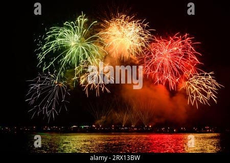 Buntes Feuerwerk und der Hintergrund des Nachthimmels mit Reflexion auf dem Wasser. Stockfoto