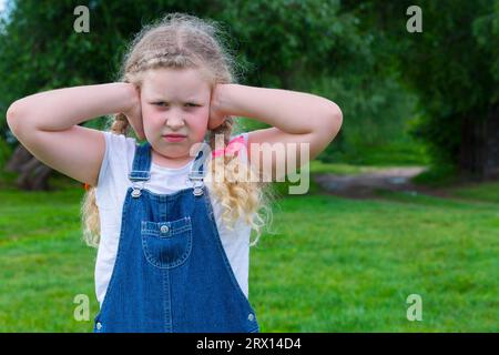 Düsteres Kind. Die verärgerten Kinderhände schließen die Ohren. Das Konzept, dem das kleine Mädchen nicht zustimmt, das Kind will nicht zuhören. Keine Bereitschaft zuzuhören, B Stockfoto