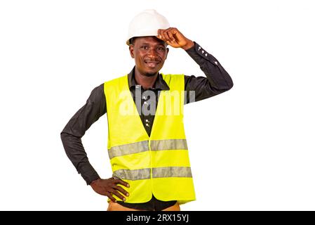 Porträt eines jungen männlichen Bauingenieurs, der Weste trägt und Hand auf weißem Sicherheitshelm hält, lächelnd. Stockfoto