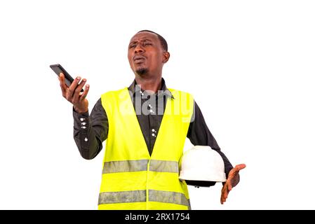 Junger Ingenieur trägt grüne Weste und Schutzhelm, während er das Handy hält. Stockfoto