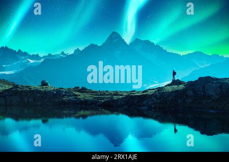 Touristen auf dem Bergsee während der unglaublichen Nordlichter von Aurora Borealis. Himmel mit Polarlichtern und Sternen hinter hohen Bergen, die sich in klarem Seewasser spiegeln Stockfoto