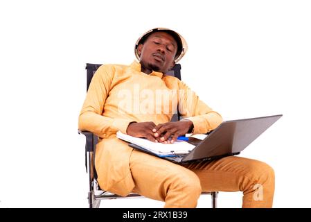 Junger, müder Architekt, Geschäftsmann, der auf einem Stuhl mit Laptop und Klemmbrett sitzt, während er schläft. Stockfoto