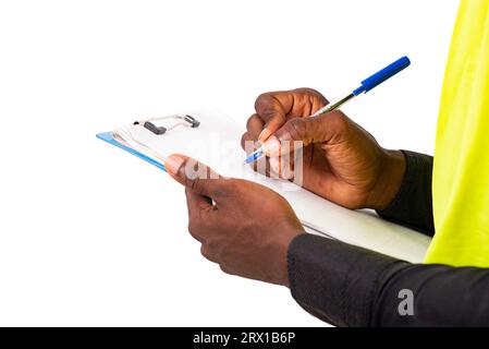 Hände eines jungen männlichen Inspektorenarchitekten, der eine grüne Weste und einen Schutzhelm trägt, während er in die Zwischenablage schreibt. Stockfoto