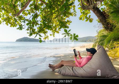 Digital Escape, eine entspannende Frau mit einem E-Book am Strand“ Stockfoto