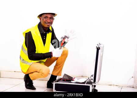 Junger glücklicher Ingenieur, der weiße Handschuhe trägt und beim Lächeln den Hammer in den Werkzeugkasten nimmt. Stockfoto