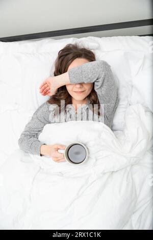 Eine müde Frau, die Kaffee im Bett trinkt Stockfoto