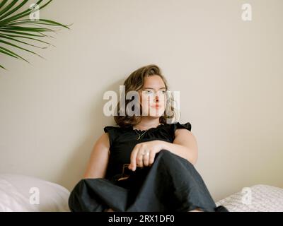 Brünette Frau in schwarzem Kleid, Brille, Handy haltend, sieht aus Stockfoto