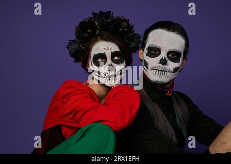 dia de los muertos-Paar, Frau in catrina-Make-up und schwarzer Kranz, der auf gruseligen Mann auf Blau lehnt Stockfoto