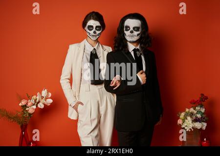 Ein Paar in catrina Make-up und Anzüge in der Nähe von festlichem DIA de los muertos ofrenda mit Blumen auf rot Stockfoto