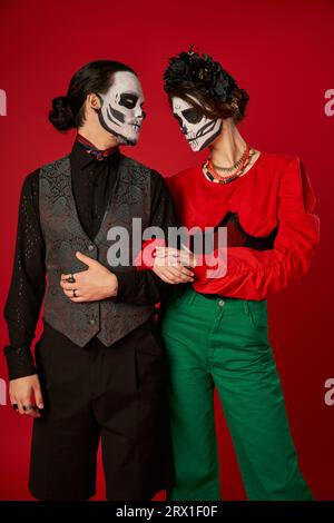 Ein Paar in trendiger Kleidung und Skelett-Make-up auf rot, DIA de los muertos Feier Stockfoto