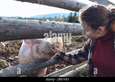 Eine junge Frau lächelt ein Schwein an und streicht es Stockfoto