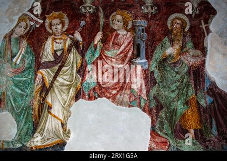 Ursula, Katharina von Alexandria und Barbara, die Symbole ihres Martyriums und Leidens tragen, zusammen mit Johannes dem Täufer. Spätgotisches Fresko in der Franziskanerkirche in Lienz, Osttirol, Österreich. Einer von zwei ehemaligen Altarbildern, die um 1440 von Nikolaus Kenntner, einem Lienzer Künstler, gemalt wurden. Stockfoto