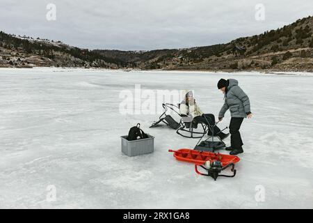 Familie auf gefrorenem See im Winter mit Schlitten und Eisangeln Werkzeuge Stockfoto