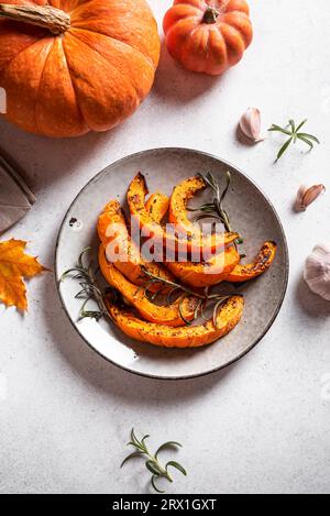 Geröstete Kürbisscheiben mit Knoblauch und Kräutern auf weißem Hintergrund. Im Ofen gebackener Kürbis, saisonale Herbstbeilage oder vegane Mahlzeit. Stockfoto