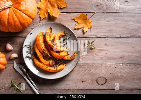 Gegrillte Kürbisscheiben mit Knoblauch und Kräutern auf hölzernem Hintergrund, Kopierraum. Im Ofen gebackener Kürbis, saisonale Herbstbeilage oder vegane Mahlzeit. Stockfoto