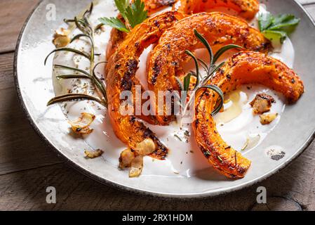 Gegrillter Kürbis mit Labneh-Joghurt und Kräutern aus nächster Nähe. Warmer, würziger Kürbissalat mit Weichkäse. Stockfoto