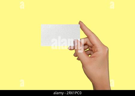 Weibliche Hand Mit Weißer Visitenkarte Isoliert Auf Gelbem Studiohintergrund. Nahaufnahme. Visitenkartenvorlage, Modell. Frauenhand mit Plastikgif Stockfoto