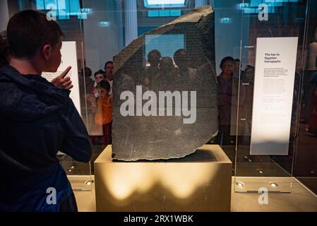 Touristen versammeln sich um den Rosetta-Stein, der im British Museum in London ausgestellt ist. Die altägyptische Stele ist der Schlüssel zur Entzifferung der Hieroglyphenschrift. Stockfoto