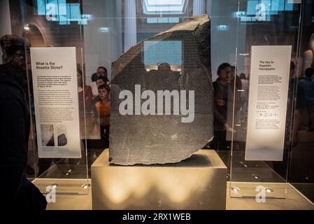 Touristen versammeln sich um den Rosetta-Stein, der im British Museum in London ausgestellt ist. Die altägyptische Stele ist der Schlüssel zur Entzifferung der Hieroglyphenschrift. Stockfoto