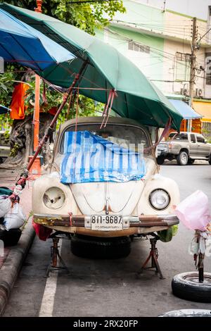 Ein sehr alter, ruinierter Volkswagen Beetle-Wagen sitzt unter ein paar Sonnenschirmen im China Town Viertel von Bangkok, Thailand. Stockfoto