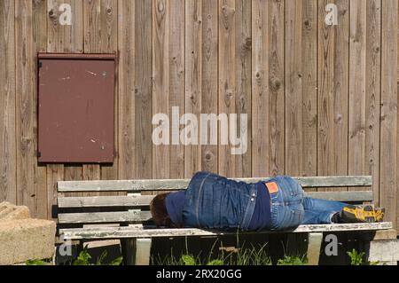 Ein müder Mann liegt auf einer Bank und ruht sich aus Stockfoto