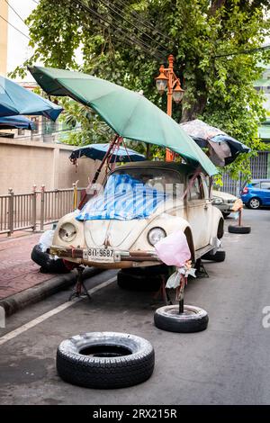 Ein sehr alter, ruinierter Volkswagen Beetle-Wagen sitzt unter ein paar Sonnenschirmen im China Town Viertel von Bangkok, Thailand. Stockfoto