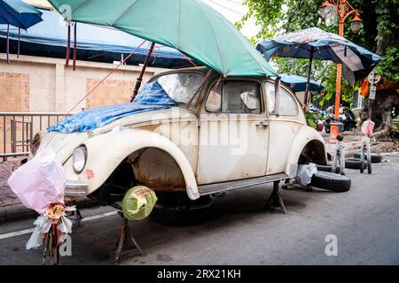 Ein sehr alter, ruinierter Volkswagen Beetle-Wagen sitzt unter ein paar Sonnenschirmen im China Town Viertel von Bangkok, Thailand. Stockfoto