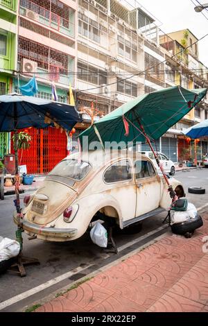 Ein sehr alter, ruinierter Volkswagen Beetle-Wagen sitzt unter ein paar Sonnenschirmen im China Town Viertel von Bangkok, Thailand. Stockfoto