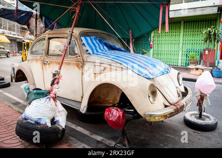 Ein sehr alter, ruinierter Volkswagen Beetle-Wagen sitzt unter ein paar Sonnenschirmen im China Town Viertel von Bangkok, Thailand. Stockfoto