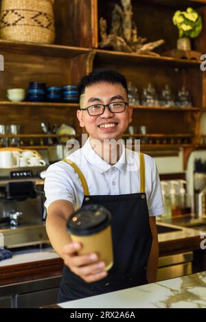 Vietnamesischer lächelnder Kellner hielt Pappbecher mit Kaffee in einem Café Stockfoto