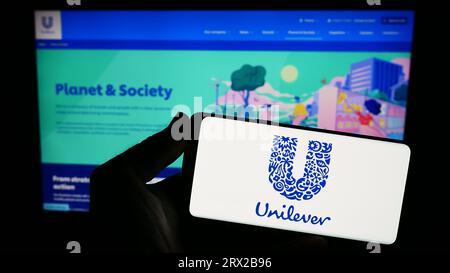 Person, die ein Mobiltelefon mit dem Logo des britischen Konsumgüterunternehmens Unilever plc auf dem Bildschirm vor der Webseite hält. Konzentrieren Sie sich auf das Display des Telefons. Stockfoto