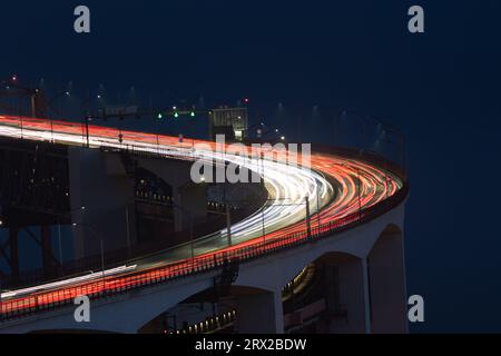 Verschwommene Lichter in Bewegung von Autofokus-Scheinwerfern, die nachts auf einer Brücke fahren. Mittlere Aufnahme Stockfoto
