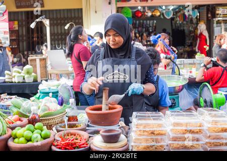 Phuket, Thailand - 25. Februar 2018: Verkäuferin von Gemüse auf dem Straßenmarkt. Muslimische Frau in Hijab kocht Soße im Basar Café Stockfoto