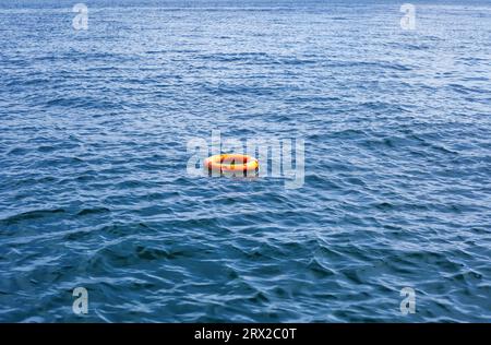 Orange lebendige Boje, die in weiten Gewässern schwimmt. Rote Rettungsschwimmer schweben auf Meereswellen. Rettungsschwimmausrüstung mit Seilschwimmen im See. Konzept der Hilfe, Stockfoto