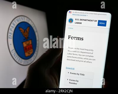 Person, die ein Mobiltelefon mit der Webseite des US-amerikanischen Arbeitsministeriums (US DOL) vor dem Siegel hält. Konzentrieren Sie sich auf die Mitte der Telefonanzeige. Stockfoto