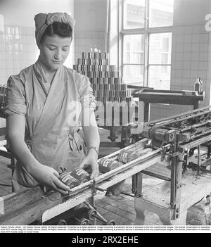 In den 1940er Jahren Inneneinrichtung aus einer Fabrik von Winborg, in der eine Mitarbeiterin an einem Förderband steht, wo Dosen, die mit bunten Etiketten versehen wurden, nach vorne Rollen. Es ist Winborgs Stachelbeercreme, die hergestellt wird, und die Gläser werden aus Qualitätsgründen sorgfältig geprüft. Schweden 1948. Kristoffersson AL48-10 Stockfoto