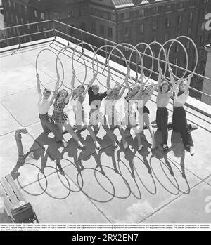 Gymnastik in den 1940er Jahren Junge Turnerinnen stehen auf einem Dach in Stockholm und bilden ein symmetrisches Bild mit den Ringen Schatten vor ihnen, wenn sie die Ringe über sich halten und sich so posieren, wie sie es tun. Schweden 1945 Kristoffersson ref O143-1 Stockfoto