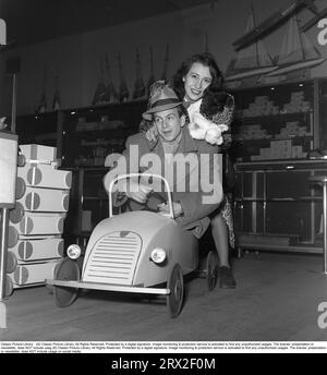 Stig Olin, 1920–2008, schwedischer Schauspieler, Filmregisseur usw. Hier mit seiner Frau Britta Holmberg auf der Suche nach Weihnachtsgeschenken im Kaufhaus NK in Stockholm und sie sind in der Spielwarenabteilung abgebildet. Er testet ein Pedalauto und seine Frau sitzt dahinter. Pedalautos waren damals ein beliebtes Spielzeug für Kinder. Schweden 1944. Kristoffersson ref L45-4 Stockfoto