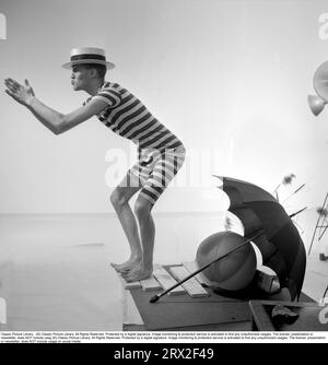 Für den Strand vorbereitet, egal welches Wetter. Der Mann ist seltsam genug gekleidet in einem historischen männlichen Badeanzug, der Anfang des 20. Jahrhunderts in einem gestreiften dunklen und hellen Muster verwendet wurde. Er trägt einen dixie-Hut und tut so, als tauche er mit seinen Händen vor ihm ins Wasser. Er ist auf schlechtes Wetter vorbereitet, wie ein Regenschirm auf dem Bild zu sehen ist. Schweden 1956 Stockfoto