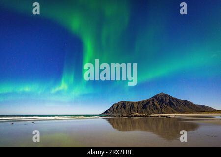 Aurora Borealis (Nordlichter) über Bergen reflektiert auf Skagsanden Strand von Wellen, Ramberg, Lofoten Inseln, Nordland, Norwegen Stockfoto